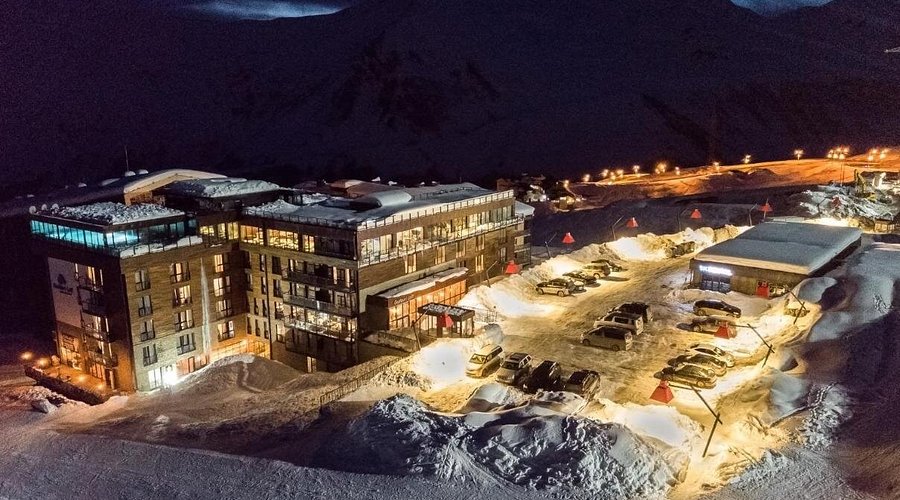 Hotellet i Gudauri oplyst i sneen om aftenen med bjerge og pister bagved